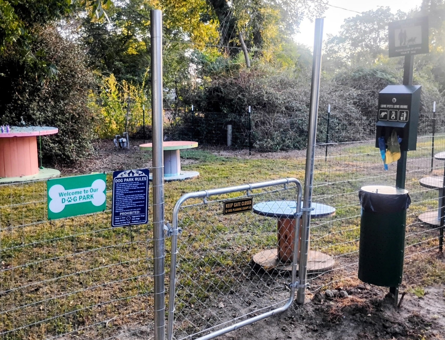 Gated dog park entrance with Welcome sign and waste bag station at Traveler's Paradise RV Park in Bay City, TX