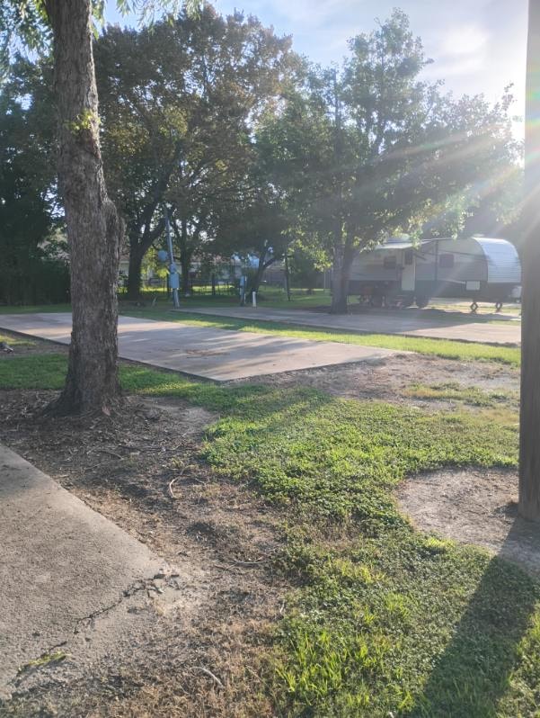 Early morning sunlight through trees over a concrete RV pad at Traveler's Paradise RV Park in Bay City, TX