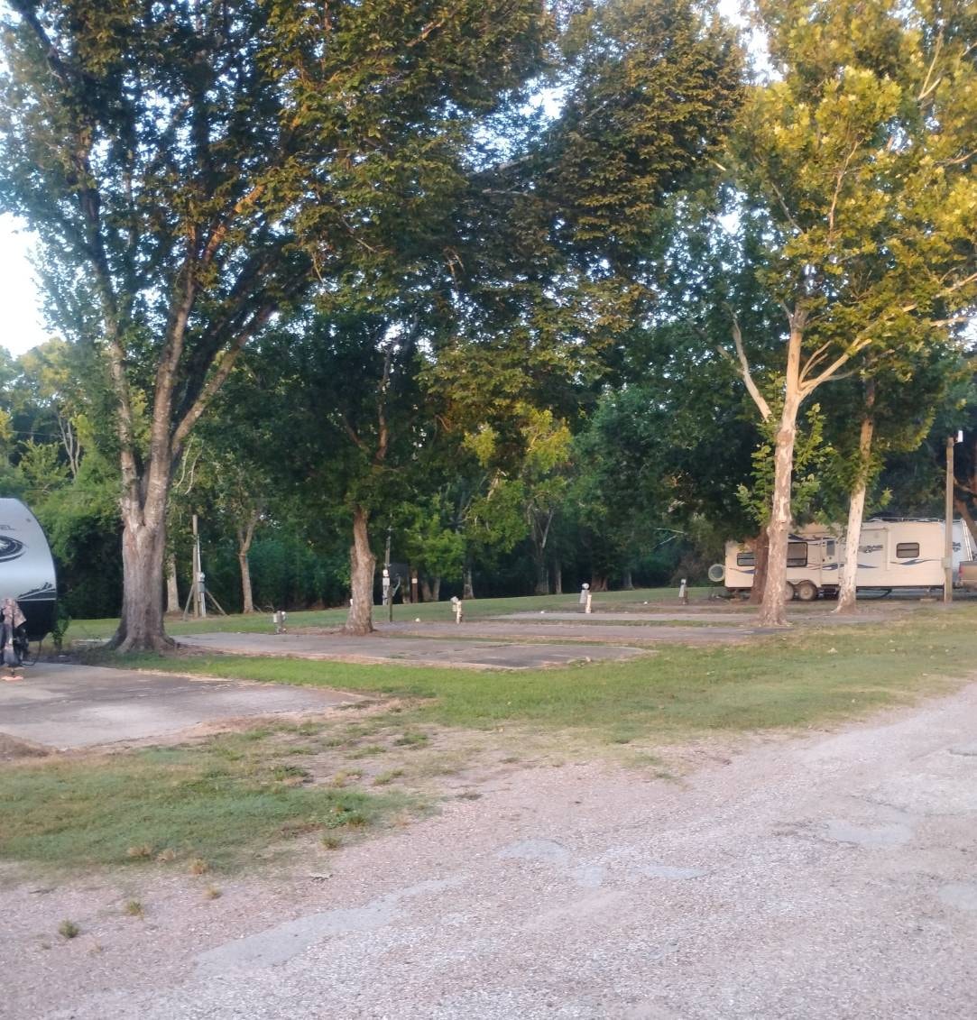 Wide shaded RV sites with utility pedestals and tall trees at Traveler's Paradise RV Park in Bay City, TX