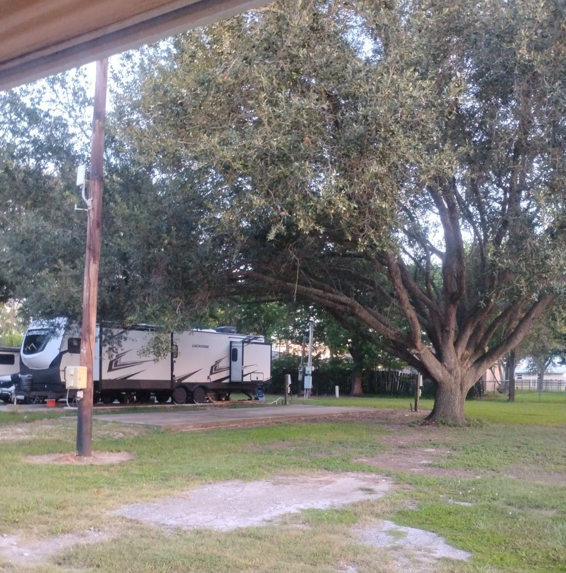 Shaded RV site with travel trailers under mature oak trees at Traveler's Paradise RV Park in Bay City, TX